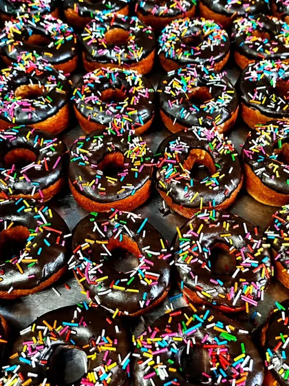 Rows of chocolate-glazed donuts carry colourful sprinkles in this close look at a sweet we offer for parties and snack boxes.