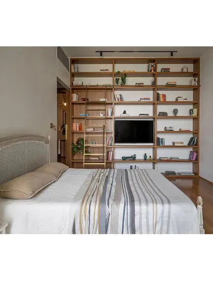 A guest bedroom featuring a floor-to-ceiling bookshelf with an integrated television and a rolling ladder. This bespoke unit provides immense storage while becoming a strong design feature.