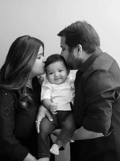 A tender moment captured in a timeless black and white family photo. The parents' kisses on their baby's head symbolize the protective and loving embrace of the family.