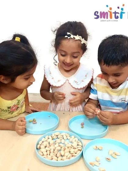 Children gather around a bowl of pistachios, carefully shelling them for their recipe. This simple task is excellent for developing pincer grasp and concentration.