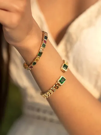A close-up of the emerald loop and multi-colored cuff bangles, showing the vibrant gemstones.