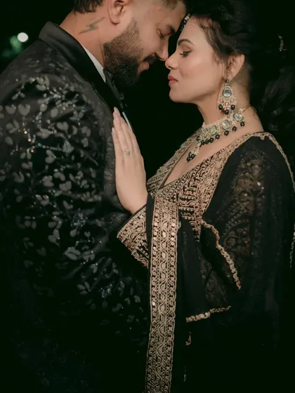 A close-up, intimate embrace, showcasing the intricate embroidery on the couple's black reception outfits.