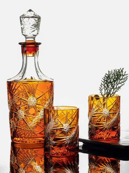 A stunning shot of an amber-colored, cut-glass decanter set against a reflective surface. The lighting is carefully controlled to make the intricate details of the glass sparkle.