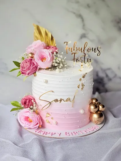 "Fabulous Forty" is the theme for this blush pink and white ombre cake. It's decorated with fresh pink flowers, gold spheres, and a touch of gold leaf for a chic and celebratory look.