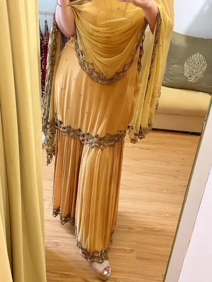 A client trying on her custom gold gharara set. The outfit features tones of gold hand-embroidered to perfection with cutwork finishing, perfect for a wedding function.