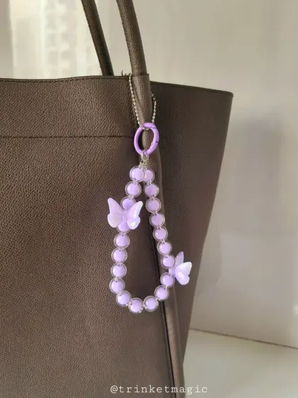 Simple, elegant, and cute. This purple beaded bag charm with butterfly accents adds a subtle pop of color and personality to a classic tote bag.