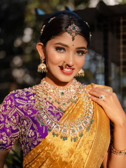 A radiant bridal portrait. The combination of the golden saree and the heavily embroidered purple blouse is regal and stunning, especially with her bright smile.
