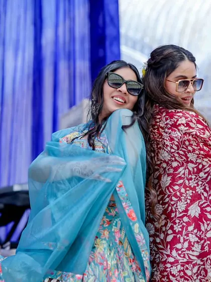 The bride and her friend posing back-to-back during their fun mehendi performance.