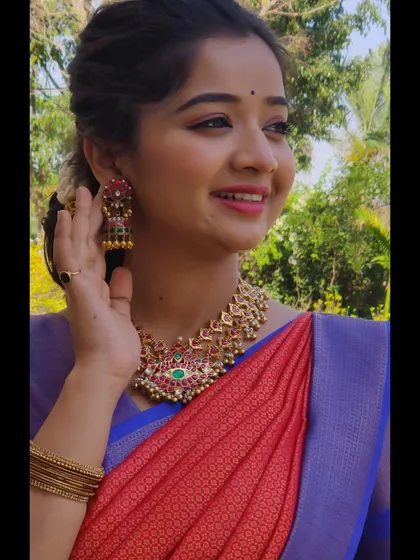 A smiling model wearing a simple kemp necklace and matching jhumkas. This is a great rental option for bridesmaids or for attending a puja.