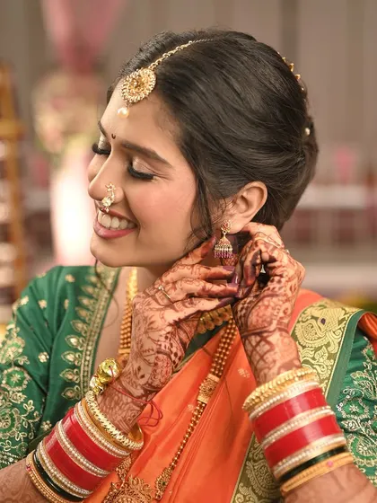 A close-up shot capturing the bride's joyful expression as she puts on her earring. This highlights the detailed eye makeup and her radiant skin.