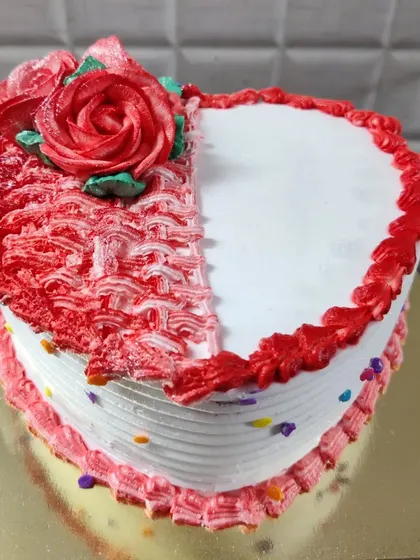 A heart-shaped cake with a half-and-half design. One side is smooth white, while the other has a textured red pattern and a buttercream rose.