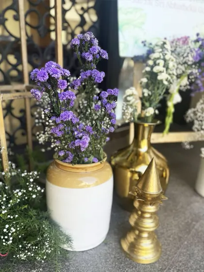 Another detail of the floral decor, showing purple statice flowers in a rustic ceramic vase next to a traditional brass temple spire (shikhar).