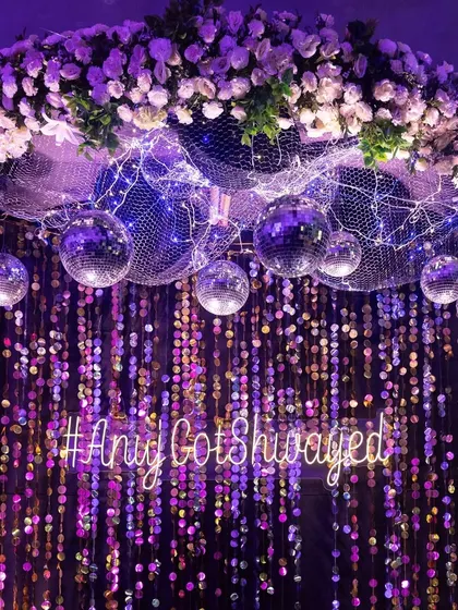 A photo booth for the sangeet, featuring a sequin backdrop, a custom neon sign with the couple's hashtag, and a floral and disco ball arrangement. It's the perfect spot for glamorous guest photos.