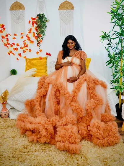 The full splendor of our peach ruffled gown is on display in this shot. The client is seated in our boho bedroom setup, with the long trail of the dress creating a stunning visual.