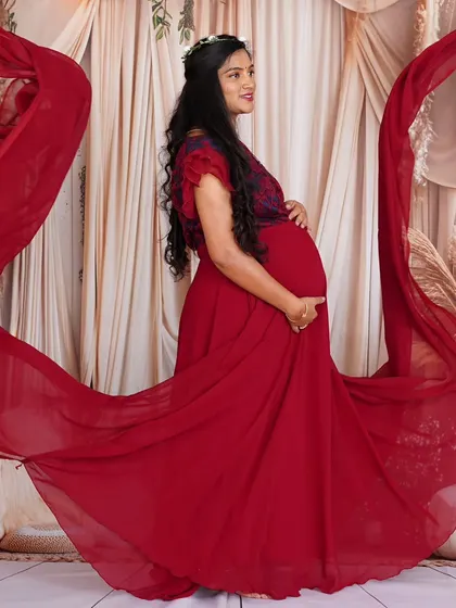The flowing red fabric of this maternity dress creates a beautiful sense of movement. The embroidered bodice adds a touch of intricate detail to the overall look.