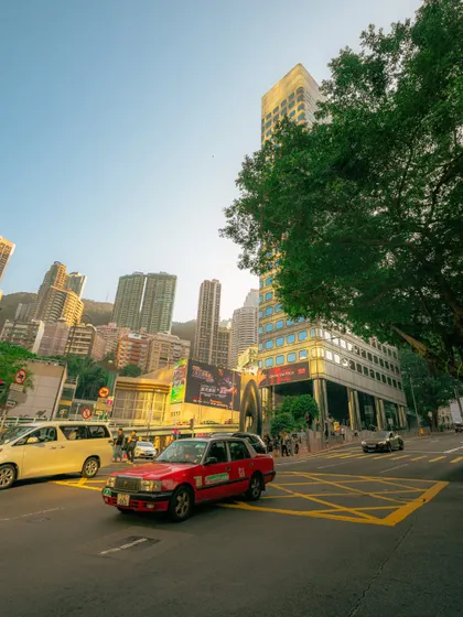 A wide-angle street scene in Hong Kong, capturing the energy of the city with its traffic and towering buildings under a clear blue sky.