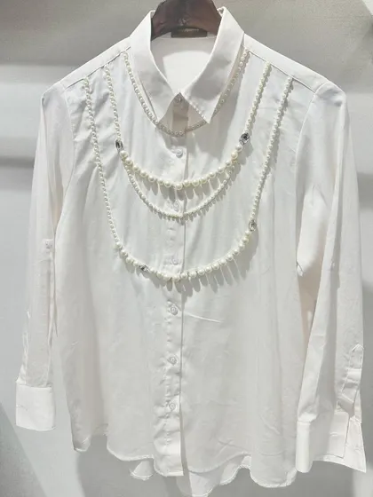It's all in the details. This classic white shirt is crafted from opulent Swiss cotton and elevated with delicate, hand-draped pearl embellishments, turning a wardrobe staple into a statement piece for lunches or evening events.