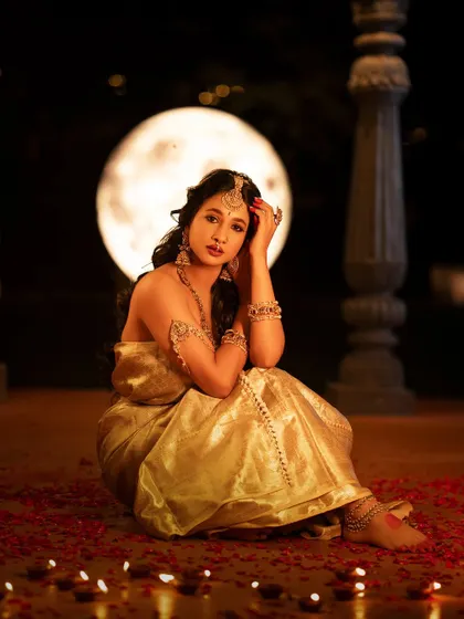 Another beautiful portrait of Manvita Kamath, seated gracefully. The golden tones of her outfit and jewelry glow in the soft light.
