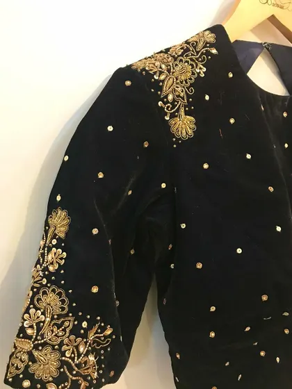 The sleeve detail of a black velvet blouse, showing the meticulous placement of sequins and the intricate floral embroidery at the cuff and shoulder.