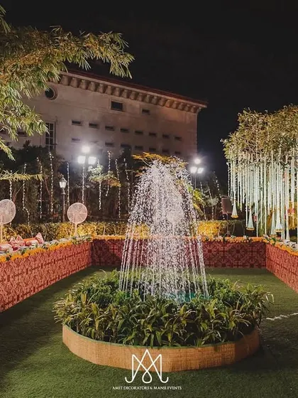 A grand traditional setup featuring a central fountain, low seating with brocade fabric, and trees adorned with hanging floral decor.