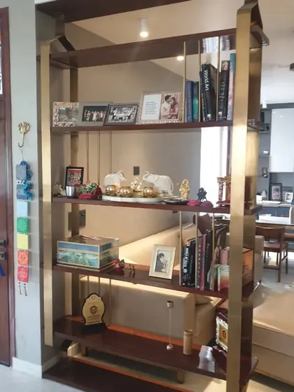 A beautiful open shelving unit made of wood and brass, used as a partition and display case. It's filled with personal decor, adding character to the home's entrance.