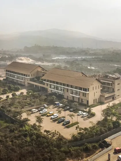 An aerial view showing the JSW Sanjeevani Hospital integrated into the industrial and rural landscape of Dolvi. The building's form and materials are chosen to be in harmony with the local context, making it a landmark for the community.