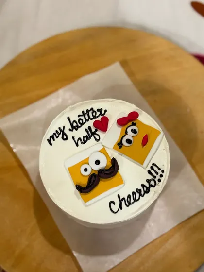A quirky and cute anniversary or couple's cake, featuring two cartoon cheese slices with the message "my better half, Cheers!!!" One slice has a mustache and the other has a bow.