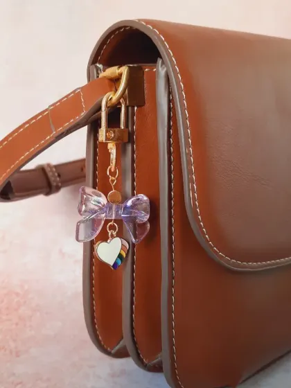 This custom bag charm features a beautiful iridescent bow and a rainbow heart, a perfect combination of elegance and pride.