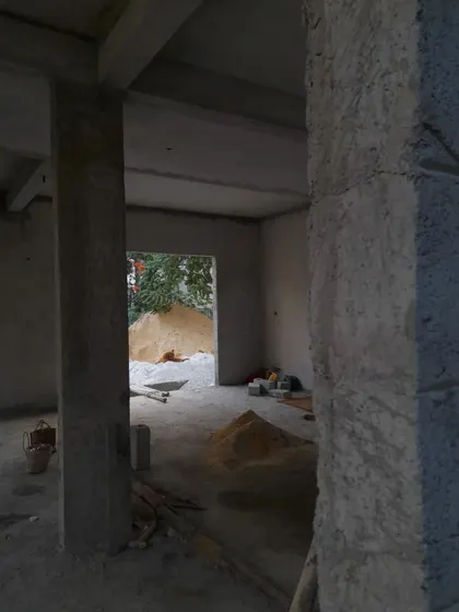 An interior progress shot showing the bare concrete columns and floors. Piles of sand wait to be mixed, a fundamental part of the building process, highlighting the raw materials that create a finished home.