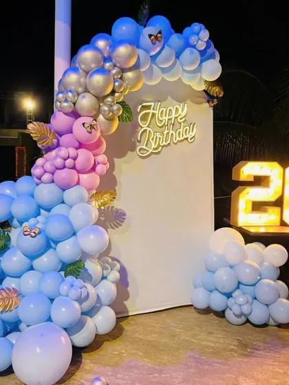 A cool and modern birthday setup with a blue and pink balloon garland and a light-up number '26'.