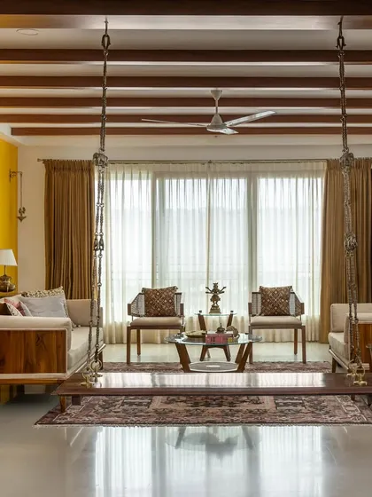 This wide view of the 'Vasudhalayah' living room highlights the expansive, open layout. The traditional swing, antique pillars, and a bold yellow accent wall come together to create a space that is both grand and deeply personal.