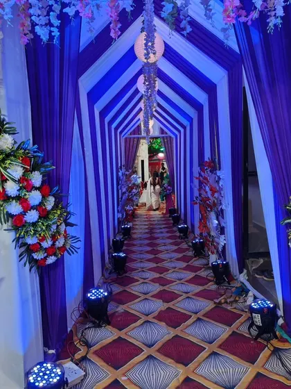 A grand entrance sets the tone for the entire event. This tunnel-style walkway, created with purple and white drapes and illuminated by spotlights, provides a stunning welcome for guests at an engagement party.