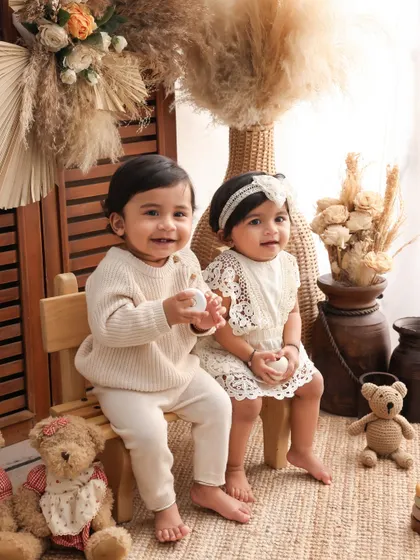 A classic portrait of the twins sitting together. Their coordinated outfits and the warm, earthy tones of the studio setup make for a beautiful and timeless image.