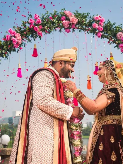 Aayush and Rashi during their Varmala ceremony under a beautiful floral arch, with the city skyline in the background.