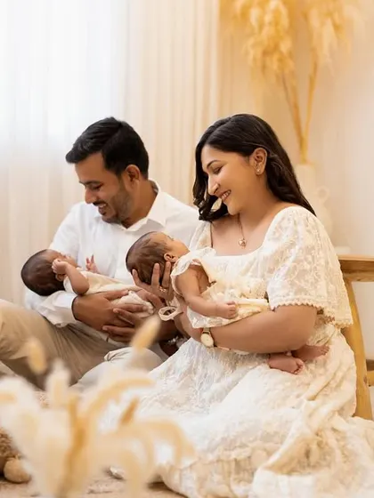 The whole family together in a relaxed, natural pose. The parents sit together, admiring their newborn twins in a bright and airy studio setting filled with soft, neutral tones.