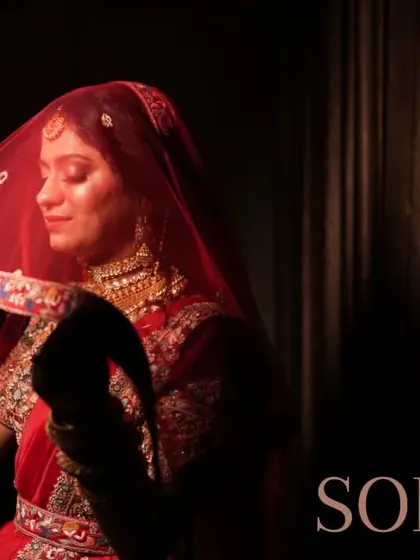 A classic bridal portrait with the bride lifting her red veil. The dark background and focused light create a dramatic and timeless effect.