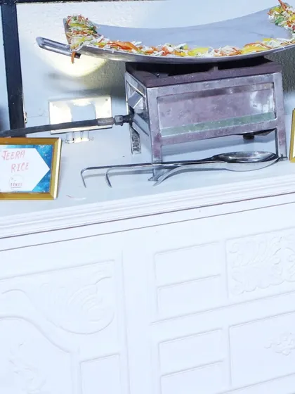 A close-up of one of my live cooking stations. This setup includes a large pan for dishes like Paneer Tava Masala, alongside labeled chafing dishes for Jeera Rice and Chicken Tikka Masala.