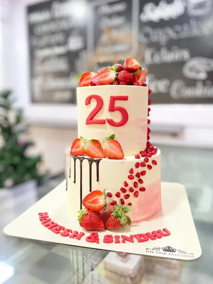 A fresh and vibrant two-tiered cake celebrating a 25th anniversary. This design features a chocolate drip, fresh strawberries, and a cascade of pomegranate seeds for a pop of color and flavor.