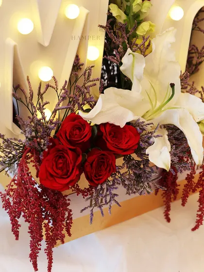 A detail shot focusing on the beautiful red roses and white lilies within the "MOM" hamper.