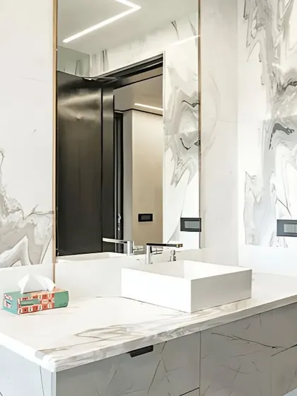 This angle shows the clean lines of the vanity in the executive bathroom. The minimalist vessel sink and sleek hardware complement the dramatic marble, while the large mirror enhances the sense of space and light.