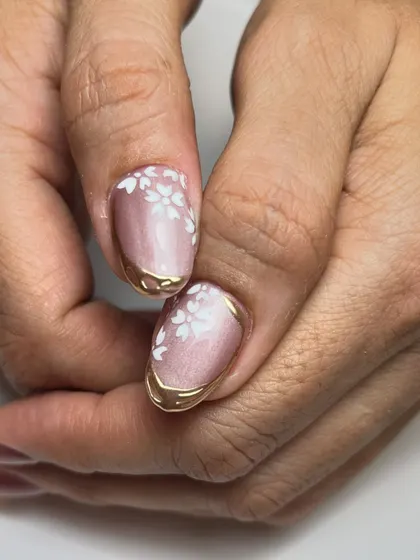 A pinch of art and a lot of glow. This design combines a soft pink cat-eye base with delicate white flowers and a bold, melted-gold chrome edge.