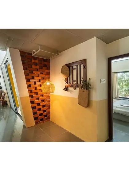 The corridor at "Aamra" features an exposed brick wall with a unique, angled bond. This detail, combined with the dual-tone oxide wall finish, showcases a commitment to material honesty and craftsmanship.