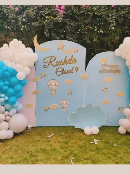A dreamy 'Cloud 9' themed outdoor birthday setup. This decoration uses custom backdrops and balloon clouds in shades of blue, grey, and white to create a heavenly atmosphere.