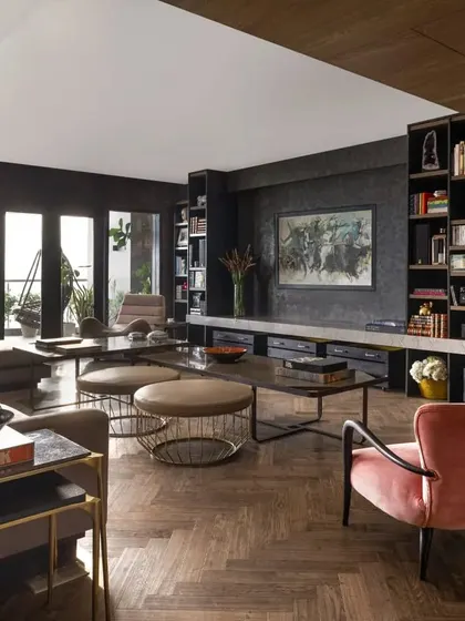 A view of the living room in the Caitriona apartment, highlighting the custom-built bookcase and media unit. The space is designed for a young professional, blending high-tech features like a retractable screen with personal touches and comfortable, stylish furniture.