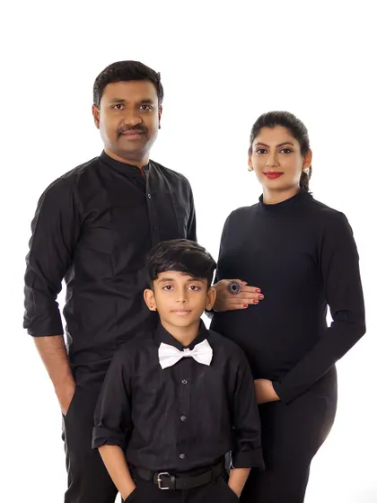 A chic and timeless family maternity portrait. The coordinated black outfits create a sophisticated look against a simple background, focusing on the family's connection.