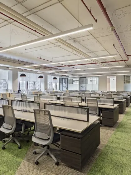 An open-plan workstation area at the Carlsberg office, designed for collaboration and flexibility. The green carpeting adds a touch of biophilic design, while the exposed ceiling and linear lighting create an industrial-chic aesthetic that is both modern and functional.
