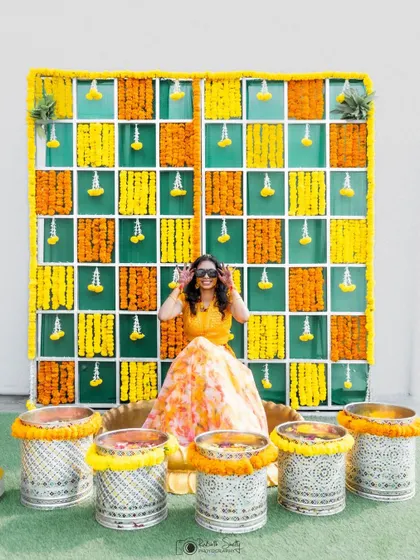 The bride making a peace sign at her Haldi ceremony. This playful pose in front of the colorful floral backdrop shows her fun personality and the happy spirit of the day.