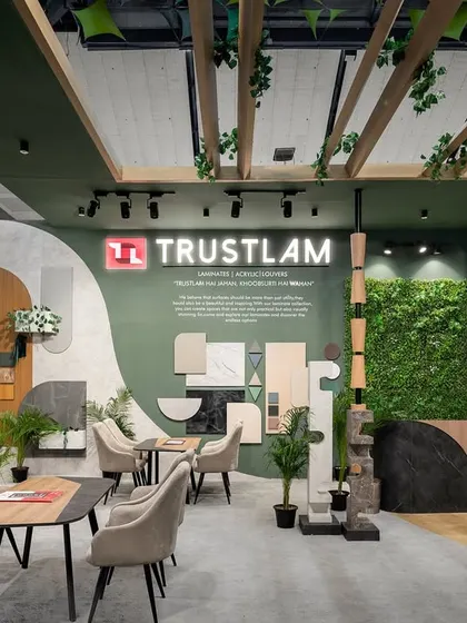 This view of the Trustlam stall highlights the use of green walls and organic shapes to create a welcoming atmosphere. The design seamlessly integrates branding, product displays, and comfortable seating areas for client conversations.