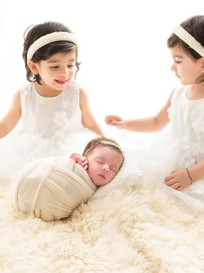 Twin sisters curiously watch over their sleeping baby sister. This image captures the wonder and sweetness of a growing family.