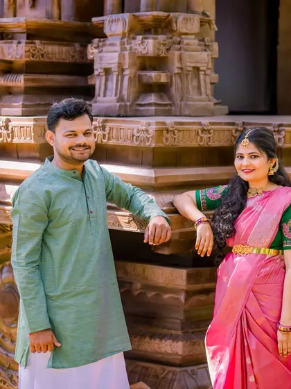 A relaxed and happy portrait of a couple by a stone chariot. Their coordinated green and pink outfits look beautiful in this classic setting.